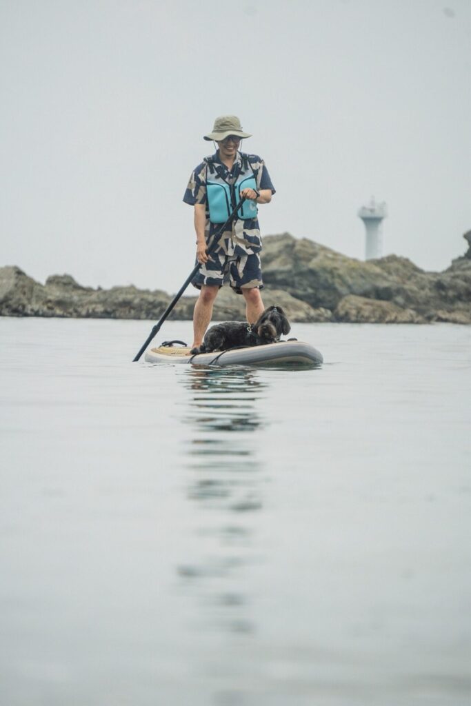 海の上でSUPボードに犬をのせて漕いでいる男性